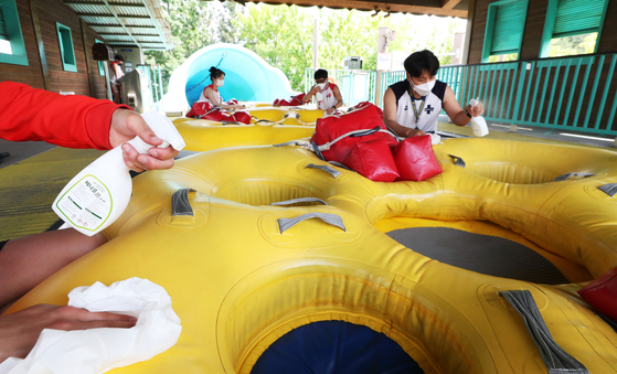 Employees from Everland, the country's largest theme park, disinfect the inflatable tubes used to ride down waterslides at Caribbean Bay on Thursday in Yongin, Gyeonggi. The water park will partially open starting Friday under strict social distancing measures. [YONHAP]