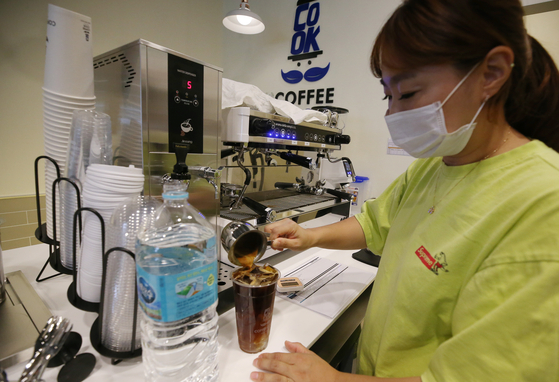 An employee at a coffee shop in Seo District, Incheon, on Thursday uses bottled water to make an Americano. The city is struggling to deal with larvae contamination in the water supply, a year after tap water was tainted due to mishandling at a treatment facility in June last year. [YONHAP]