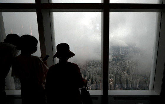 Visitors look at apartments in Jamsil covered in fog from Lotte Tower in Songpa, southern Seoul, on Monday. As the ruling Democratic Party (DP) is planning to push through the government’s hike of property taxes with the 176 seats it has in the National Assembly, the government is expected to announce its housing supply plan. Despite the government’s efforts, apartment prices in Seoul continued to rise. According to the Korea Appraisal Board, Seoul apartment prices in July rose 1.12 percent compared to June despite the government rolling out new real estate measures. [YONHAP]