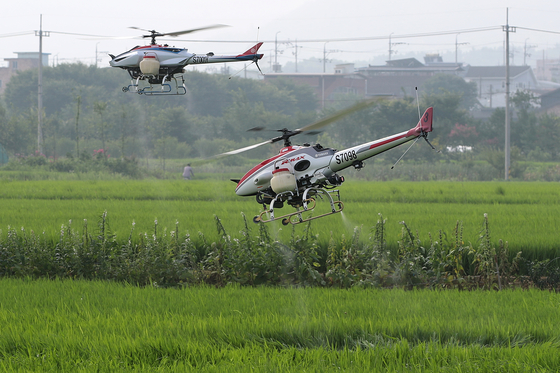 Two unmanned helicopters spray pesticide over a rice paddy in Dalseong County, Daegu, on Tuesday. The county office decided to offer free pest control to rice farms covering 2,683 acres due to a shortage of labor. [NEWS1] 