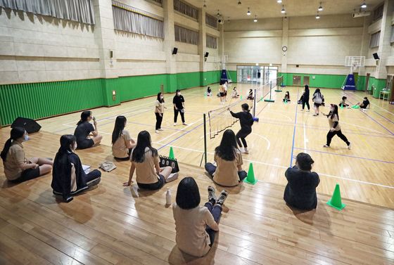 Students in face masks play badminton during a physical education class. [PARK SANG-MOON]