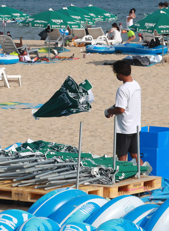 A man organizes parasols at Haeundae Beach, Busan, on Thursday afternoon after the government announced that seven public beaches in the city, which were to open until the end of the month, will be closed amid concerns over the spread of Covid-19. Visitors can still enter the beaches, but parasols, toilets and showers are unavailable. [YONHAP]