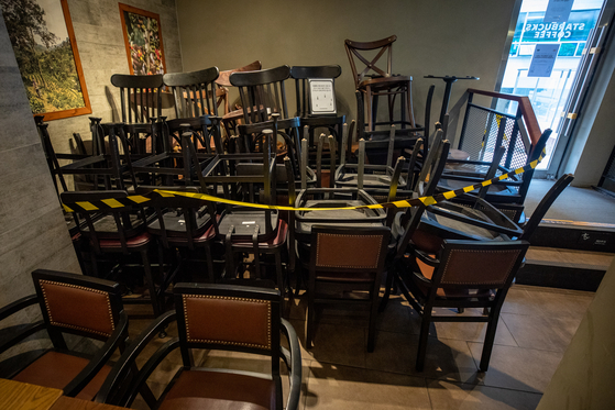 Tables and chairs are stacked at a coffee shop chain in downtown Seoul Sunday, the first day that the Seoul metropolitan area fell under more restrictions from the central government’s three-tier social distancing system. [NEWS1]