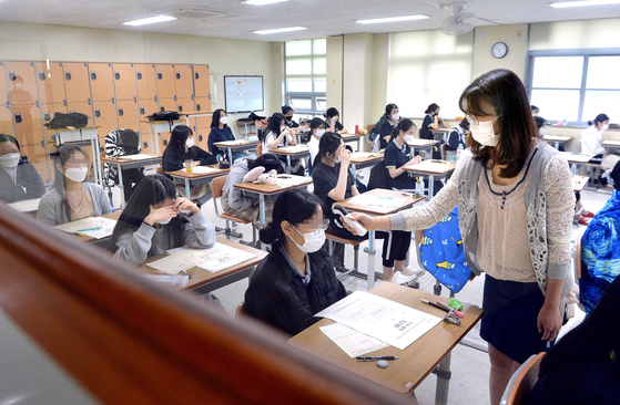 A teacher measures body temperatures of students before they take a trial college entrance examination in Dunwon High School in Daejeon on Wednesday. Around 480,000 students across the country applied for the mock exam, 11.3 percent less than the number last year.  [KIM SEONG-TAE]