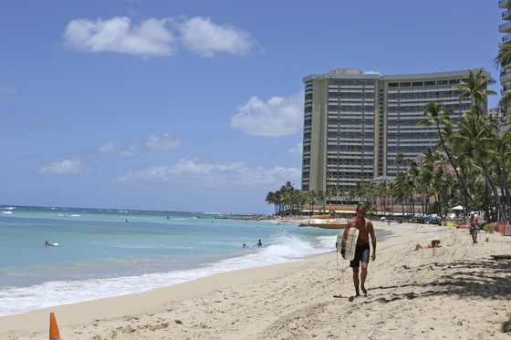 In this June 5, 2020, file photo, a surfer walks on a sparsely populated Waikiki Beach in Honolulu. Hawaii's governor says that starting Oct. 15, travelers arriving from out of state may bypass a 14-day quarantine requirement if they test negative for Covid-19. [AP/YONHAP]