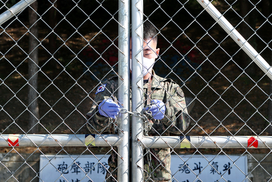 A masked soldier locks the front gate of a Korean Army unit in Pocheon, Gyeonggi, on Monday after 36 Covid-19 cases were confirmed there. [YONHAP]