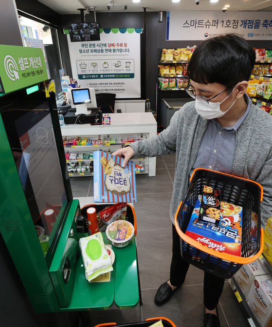 A government official demonstrates how to use the self-payment counter at Korea's first unmanned supermarket in Dongjak District, southern Seoul on Thursday. The supermarket is operated without human supervision only at night and has smart gates, self-cashiers and security systems installed to prevent theft. The Small Enterprise and Market Service and the Ministry of SMEs and Startups plan to expand the introduction of such "smart supermarkets" next year. [YONHAP]