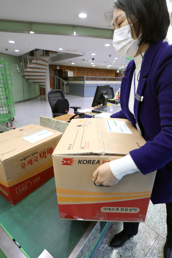 A Korea Post employee lifts up a packaged box with two holes to help delivery workers lift boxes on Monday at the institution's headquarters in Jung District, central Seoul. The government and Korea Post started selling boxes with holes in each side, which could reduce a package's load by 10 percent and ease the physical burden for delivery workers. [YONHAP]