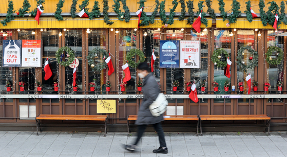 A pedestrian passes a restaurant decorated with Christmas ornaments in the neighborhood of Hongik University in Mapo District, western Seoul, on Monday. As the Level 2.5 social distancing measures are imposed in the capital area, shopkeepers worry that year-end revenues will vanish. [YONHAP]