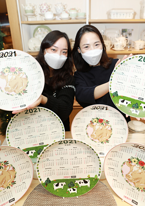 Models pose with dishes showing the 2021 calendar and images of white oxen, made by ceramic company ZEN, at Lotte Department Store’s headquarters in central Seoul on Monday. According to the lunar calendar, 2021 is the year of the white ox, signifying peace and leisure. [YONHAP] 
