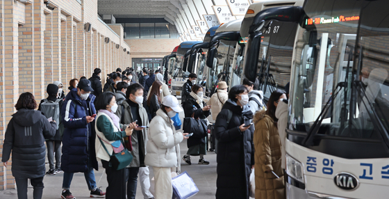 People wearing masks board buses at the Express Bus Terminal in Seocho District, southern Seoul, on Wednesday, to spend the Lunar New Year holidays with their relatives. The number of people traveling is expected to be much less this Lunar New Year because of the Covid-19 pandemic. [YONHAP]