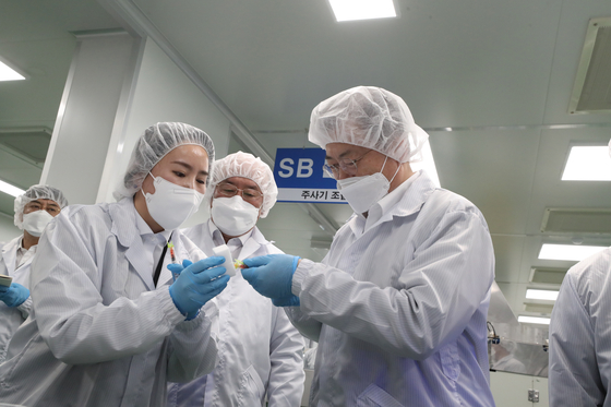 President Moon Jae-in, right, examines "low dead space (LDS)" syringes designed to reduce the dead space between the needle and the body, to be used in Covid-19 vaccinations to minimize waste in dosages, at PoongLim Pharmatech in Gunsan, North Jeolla Thursday. [JOINT PRESS CORPS]
