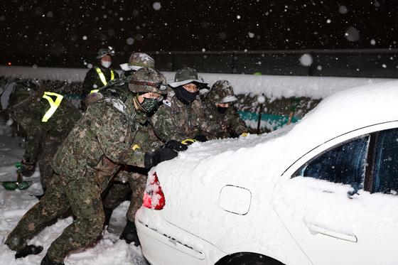 Soldiers from the 8th Army Corps and 102nd Armored Brigade push a car stuck on the road during a snowstorm Monday in Sokcho, Gangwon. [NEWS1]