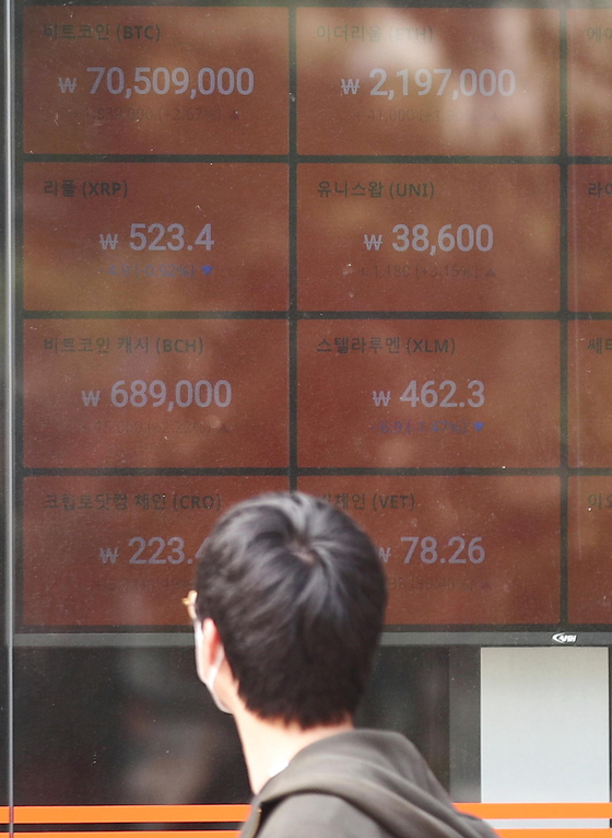 A passerby looks at cryptocurrency prices displayed on a screen operated by local cryptocurrency exchange Bithumb in Gangnam, southern Seoul, on Sunday. The price of bitcoin surpassed 70 million won ($62,000) for the first time on Sunday and went as high as 71 million won. [YONHAP]