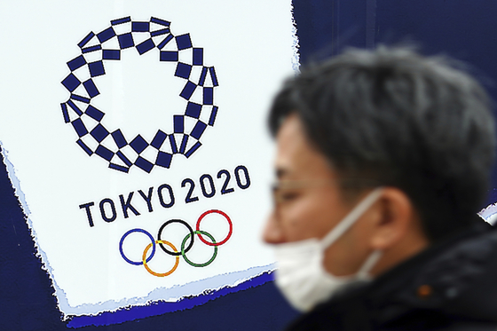 A man wears a protective mask to help curb the spread of the coronavirus near the logo of the Tokyo 2020 Olympic Games. [AP/YONHAP] 