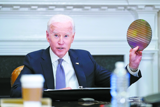 President Joe Biden holds up a silicon wafer as he participates virtually in the CEO Summit on Semiconductor and Supply Chain Resilience at the White House on April 12. [AP]