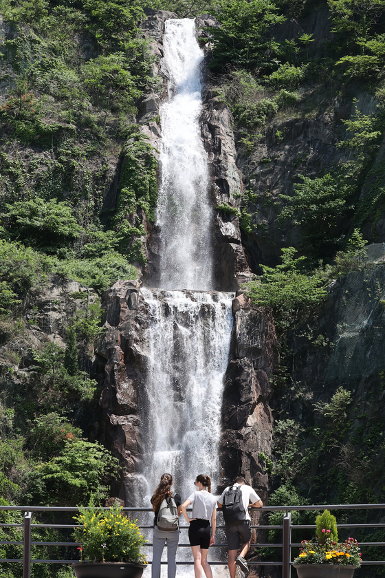 People in summer clothes appreciate a large-scale artificial waterfall at the foot of Mount Yongma in Jungnang District, eastern Seoul, on Wednesday in the warm weather reminiscent of early summer. [NEWS1]