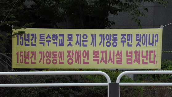 A still image from the film ″A Long Way to School″ shows placards in protest of the construction of Seojin School hanging in the streets of Gayang-dong, western Seoul, one of which reads, ″Is it the Gayang-dong residents' fault that no special-needs school has been built in 15 years? In 15 years, Gayang-dong is flooding with welfare facilities for people with disabilities.″ [JINJIN PICTURES]