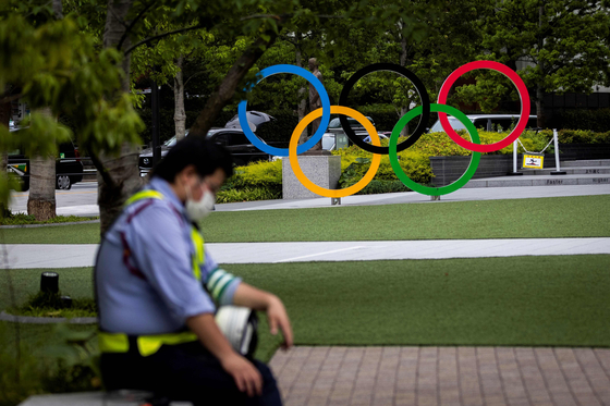 A security guard takes a break in front of the Olympic rings in Tokyo on June 3, 2021.  [AFP]