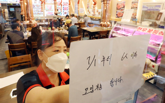 An employee puts up a notice on the wall of a restaurant in Myeong-dong, central Seoul, on Monday, to inform customers of eased social distancing guidelines that will allow private gatherings of up to six people from July in the greater Seoul area. [YONHAP]