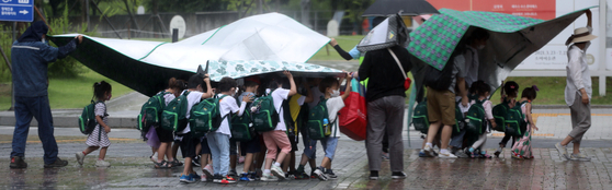 Kindergartners take refuge under their picnic mats during sudden showers on Tuesday afternoon at a park in Seoul. [YONHAP] 