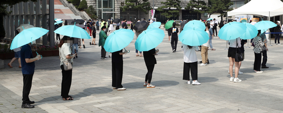 Shielding themselves from the sun, people wait in line to take Covid-19 tests in Incheon on Monday as Level 4 social distancing rules are imposed. [YONHAP]