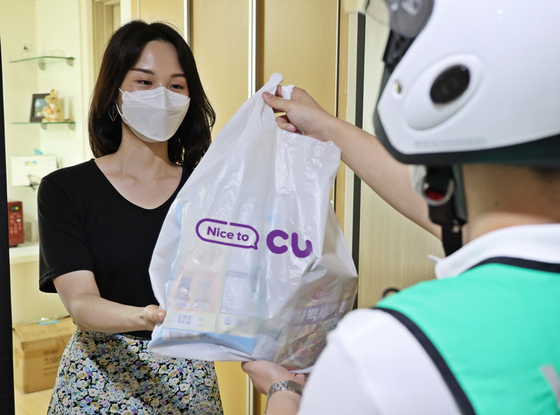 A model receives products she ordered via CU’s quick commerce service from a delivery rider. [BGF RETAIL]