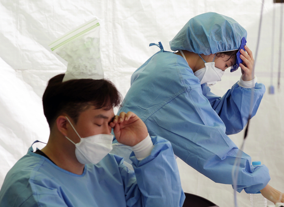 Medical workers cool themselves off with ice at a Covid-19 testing site in Yangcheon District, western Seoul, on Thursday. [YONHAP]