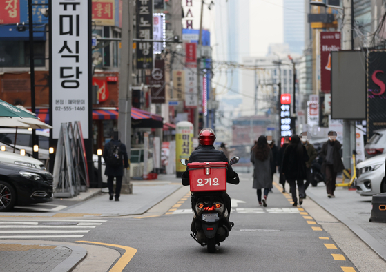 A Yogiyo food delivery passes by restaurants in Gangnam District, southern Seoul during lunch hour last December. [YONHAP] 