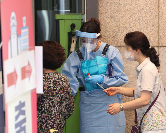 A medical worker wears ice packs while carrying out tests at a Covid-19 testing station in Dongjak District, southern Seoul, on Thursday, amid a heat wave. [NEWS1]