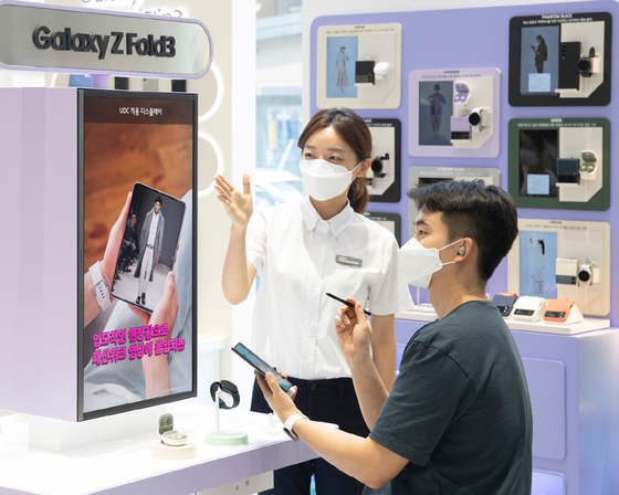 A customer tests the new Galaxy Z Fold 3 at the Samsung Digital Plaza Hongdae branch in western Seoul on Monday with the help of a staff member. Samsung Electronics will start accepting orders for its new Galaxy Z Fold 3 and Galaxy Z Flip 3 foldable smartphones for a week starting Tuesday. Sales begin on Aug. 27. [SAMSUNG ELECTRONICS]