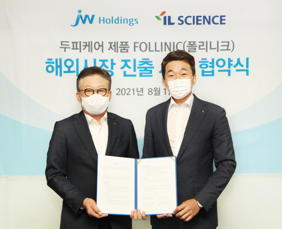 JW Holdings CEO Han Seong-gwon, left, and IL Science CEO Song Seong-geun pose for a photo after signing a memorandum of understanding for selling Follinic’s haircare products overseas at its headquarters in Seocho-dong, southern Seoul, on Tuesday. [JW HOLDINGS] 