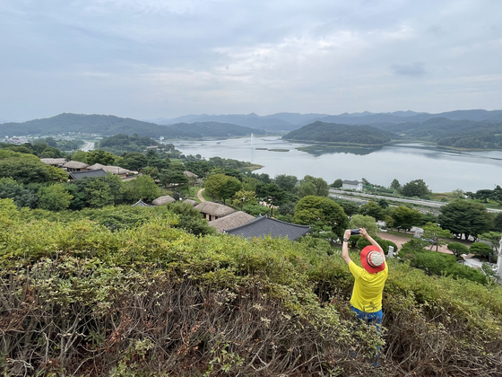 A visitor to Munui Cultural Heritage Complex, also known as Munui Cultural Properties Site, takes a photo of the manmade village that features hanok with hay-thatched or giwa tiled rooves. It is also possible to view the Daecheong Reservoir, which was made with the establishment of the Daecheong Dam. Many of the houses where moved to this location because of fears that they would be flooded by the dam. [LEE SUN-MIN]