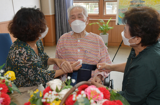 Two daughters hold hands with their father Lee Joo-hwan, 93, at a nursing home in Suwon, Gyeonggi, on Monday. Starting Monday, the government temporarily allowed patients and visitors to meet face-to-face if both are fully vaccinated — part of special virus control measures to be applied for the Chuseok holidays until Sept. 26. [NEWS1]
