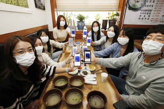 Officials from a public health center in Gwangju produce certificates that show they have been fully vaccinated on their mobile phones on Friday as they have lunch together. Under the slightly eased social distancing guidelines applied from Monday for the next two weeks, the cap for social gatherings after 6 p.m. will be increased from the current six people to a maximum of eight, as long as no more than four in a group are unvaccinated, in the metropolitan area of Seoul, Gyeonggi and Incheon. This includes gatherings at restaurants, cafes and multi-use facilities. A maximum of 10 people, again with no more than four unvaccinated people, will be allowed to meet outside of greater Seoul starting Monday. [YONHAP]