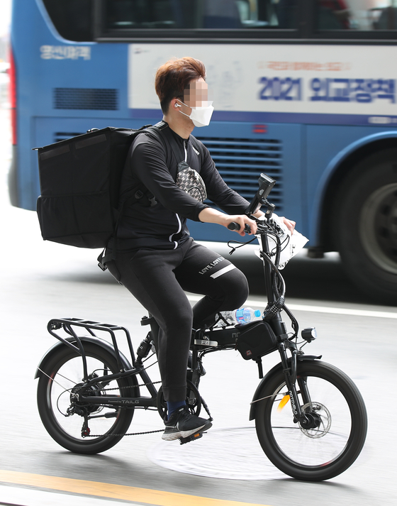 A delivery worker rides an electric bike on a street in Jongno, central Seoul on July 12. [YONHAP] 
