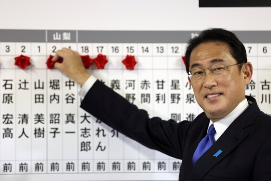 Japan's prime minister and ruling Liberal Democratic Party leader Fumio Kishida puts rosettes above the names of successful general election candidates on a board at the party headquarters in Tokyo on Oct. 31. [BEHROUZ MEHRI/AP/YONHAP]