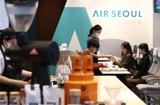 An Air Seoul employee serves inflight food at Coffee Bean's branch in Gwanghwamun, Seoul, that was redecorated to resemble the inside of a plane on Tuesday. The budget airline said it has joined hands with the coffee company to provide inflight experiences for customers who are longing for overseas trips since the Covid-19 pandemic started. Thanks to the growing number of people receiving vaccinations across the world, some countries have been opening their boarders, but the upsurge of daily cases in several countries including those in Europe means restrictions have been re-implemented, a blow to the travel industry. [YONHAP] 