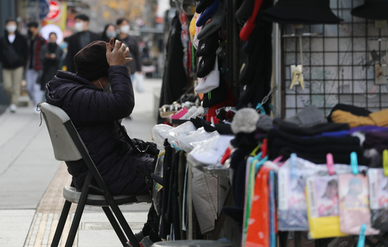 A street vendor sits in front of her stall in Itaewon, Seoul, on Sunday. Despite the government's relaxed social distancing regulations implemented earlier this month, the growing number of new daily cases of Covid-19 along with growing concerns of the new Omicron variant, is leaving many small business owners worried. [YONHAP]