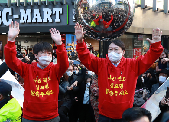 Lee Jun-seok, left, chief of the main opposition People Power Party (PPP), and Yoon Seok-youl, the party’s presidential nominee, wave to the crowd in matching red hoodies in the streets of Busan Saturday, after their reconciliatory dinner meeting in Ulsan the night before. [YONHAP]