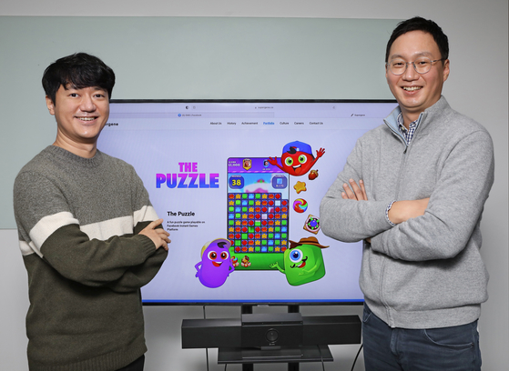 Na Young-chae, left, and Lee Chin-ho, co-CEOs and founders of Supergene, stand before a screen featuring Supergene's social game "The Puzzle" at its office in Pangyo, Gyeonggi. [PARK SANG-MOON]