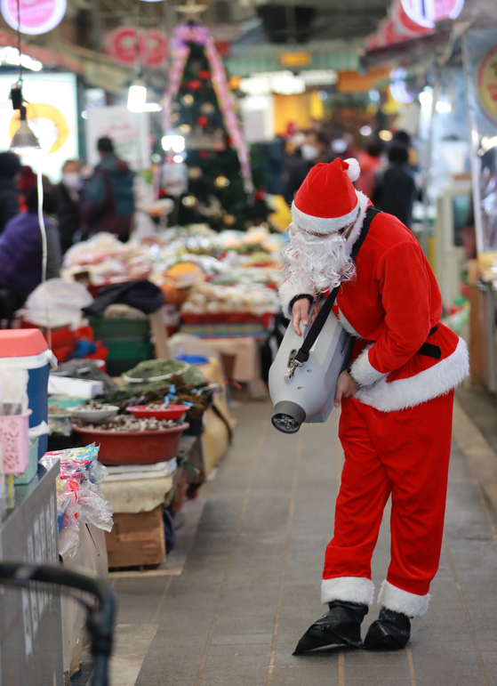 A man dressed in a santa suit disinfects Seodong Maze Market in Geumjeong District, Busan, on Monday. The "2021 Christmas Market" will be held at 35 Busan traditional markets, including the Seodong Maze Market, through Dec. 26. Various discounts and events will be held for people who visit the markets. [YONHAP]