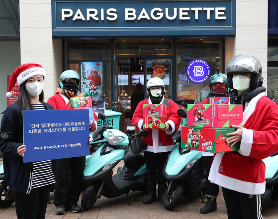 Baedal Minjok delivery workers hold up Christmas presents for children at child welfare agencies in Seoul at a Paris Baguette branch in Myeong-dong, central Seoul, on Tuesday. Baedal Minjok and Paris Baguette partnered with the ChildFund Korea to facilitate the gift. [YONHAP]