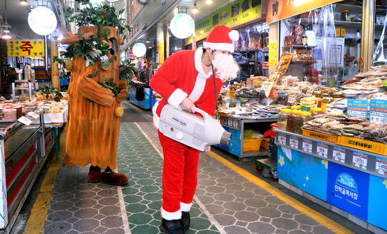 A man dressed in a Santa Claus costume disinfects an outdoor market in Busan on Thursday as Christmas draws near. [SONG BONG-GEUN]