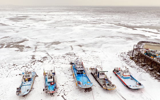 Fishing boats settled on frozen seawater at Yeongjong Island, Incheon, on Monday, as temperatures stayed below freezing across the country. [YONHAP]