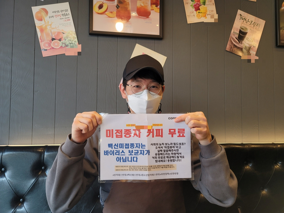 Kim Jong-min, the owner of a cafe in Bucheon, Gyeonggi, holds a paper notice saying “The unvaccinated are not virus carriers.” Kim has been offering free coffee to people who are not vaccinated, and said he will continue to do so until the government withdraws the vaccine pass policy. [HAM MIN-JUNG]  