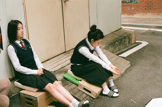 In the early 2000s, tight, short blouses and wide, long skirts of mid-shin length was a popular look among female students, shown right. This is a scene from the movie ″Snowball″ (2021), which is set in the 2000s. [ATNINE FILM]