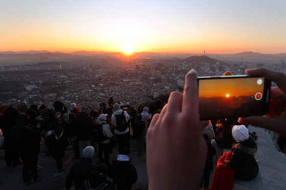 People watch the first sunrise of 2022 from the top of Mount Inwang in central Seoul on Saturday. [YONHAP]
