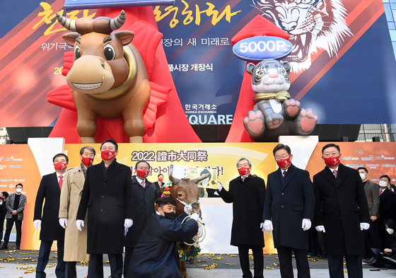 Presidential candidates Yoon Suk-yeol of the People Power Party, front left, and Lee Jae-myung of the Democratic Party, front right, pose with a banner and an inflatable bull and tiger in front of the Korea Exchange building in Yeouido on Monday to celebrate the opening of the stock exchange for the first time this year. The Kospi ended its first session of the year favorably, gaining 11.12 points, or 0.37 percent from the last trading day of 2021. [JOINT PRESS CORPS] 