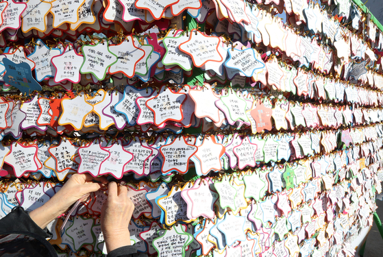 Visitors to Jogye Temple in Jongno District, central Seoul, on Tuesday write their wishes on star-shaped paper and hang them on a wall set up in the yard. [KANG JUNG-HYUN]